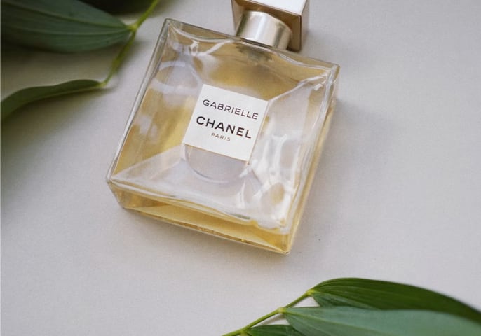 Gabrielle channel Essence de perfume bottle lying on table with leaves above and below it
